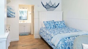 Una camera da letto con un letto, una testiera bianca, un quadro e vista sul bagno.