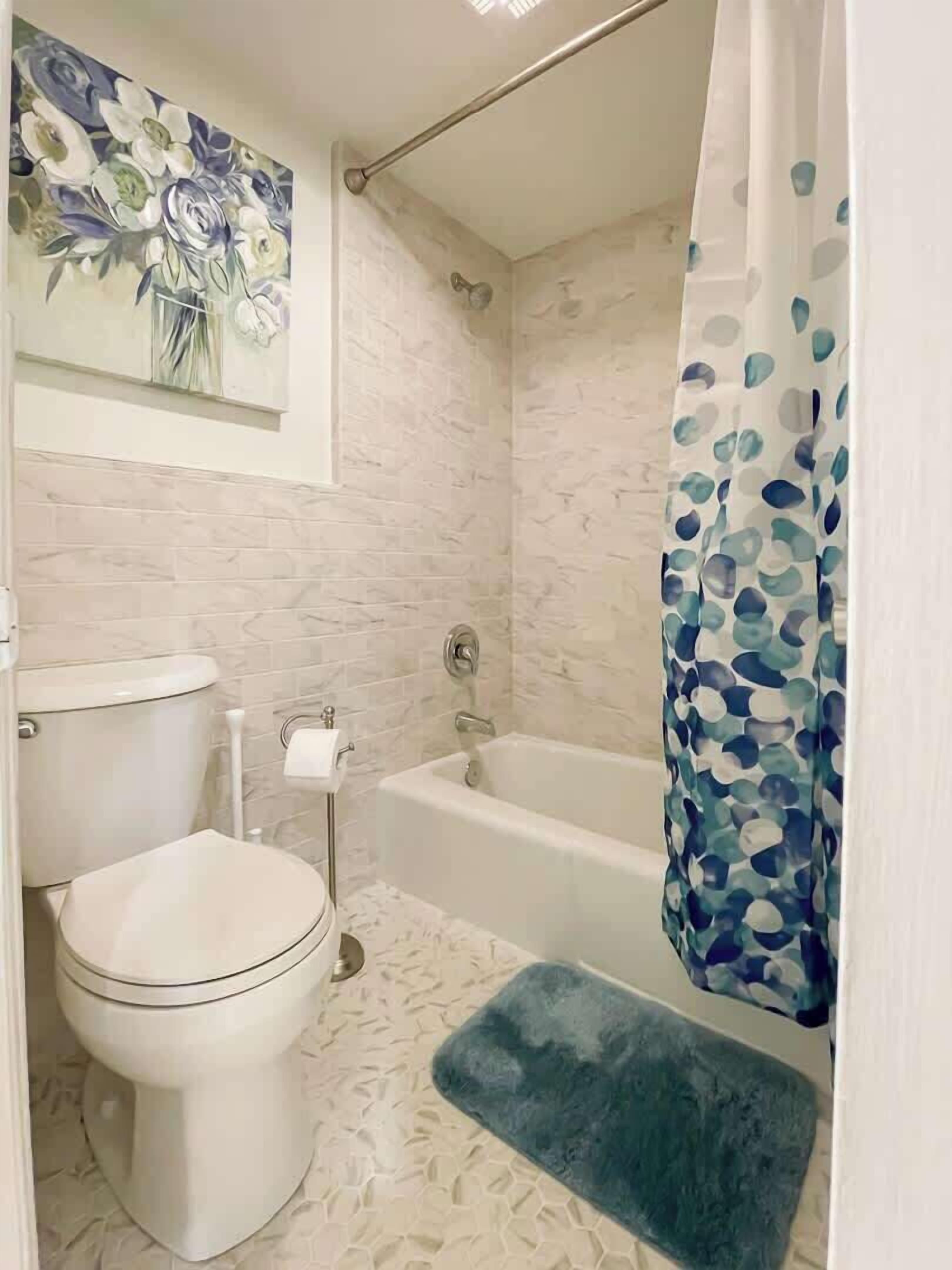 A bathroom with a toilet, a bathtub, a shower curtain, and a decorative painting on the wall.