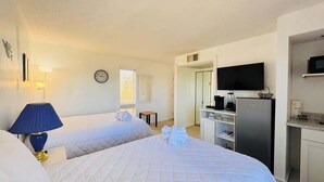 Ein Hotelzimmer mit zwei Betten, einem Fernseher, einem Kühlschrank und einem Schreibtisch.