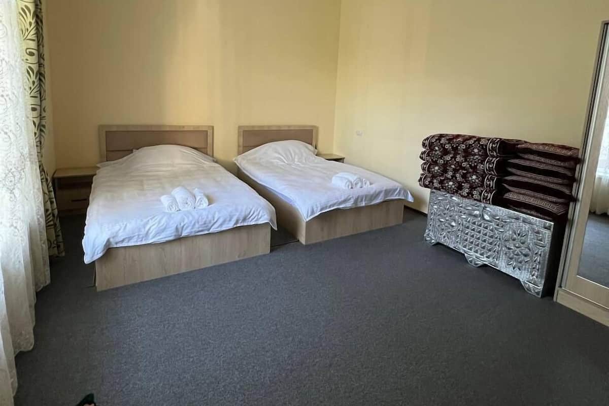 A hotel room with two single beds, a chandelier, an air conditioning unit, a patterned sofa, and a mirror.