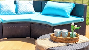 A curved wicker sofa with light blue cushions, a woven tray with cups and a vase of white flowers, and a woven table runner. - ClickSardegna Villa Lucilla with swimming pool (Alghero)