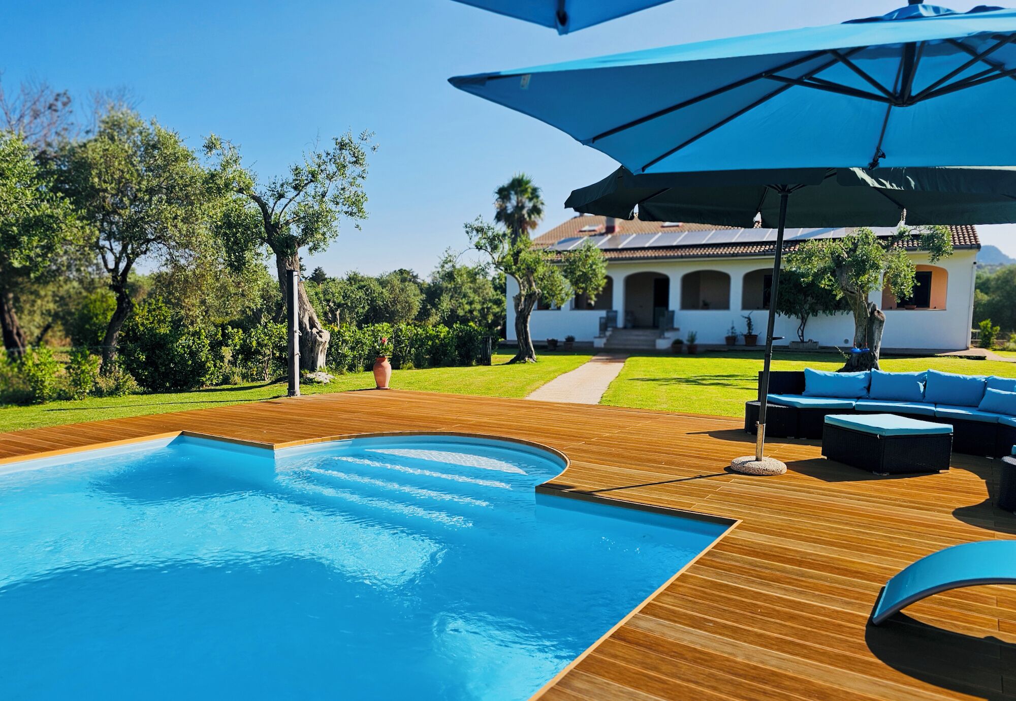 A swimming pool with wooden decking, outdoor furniture, and umbrellas.