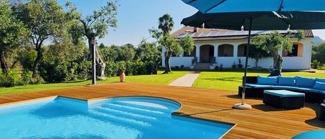 A swimming pool with wooden decking, outdoor furniture, and umbrellas.