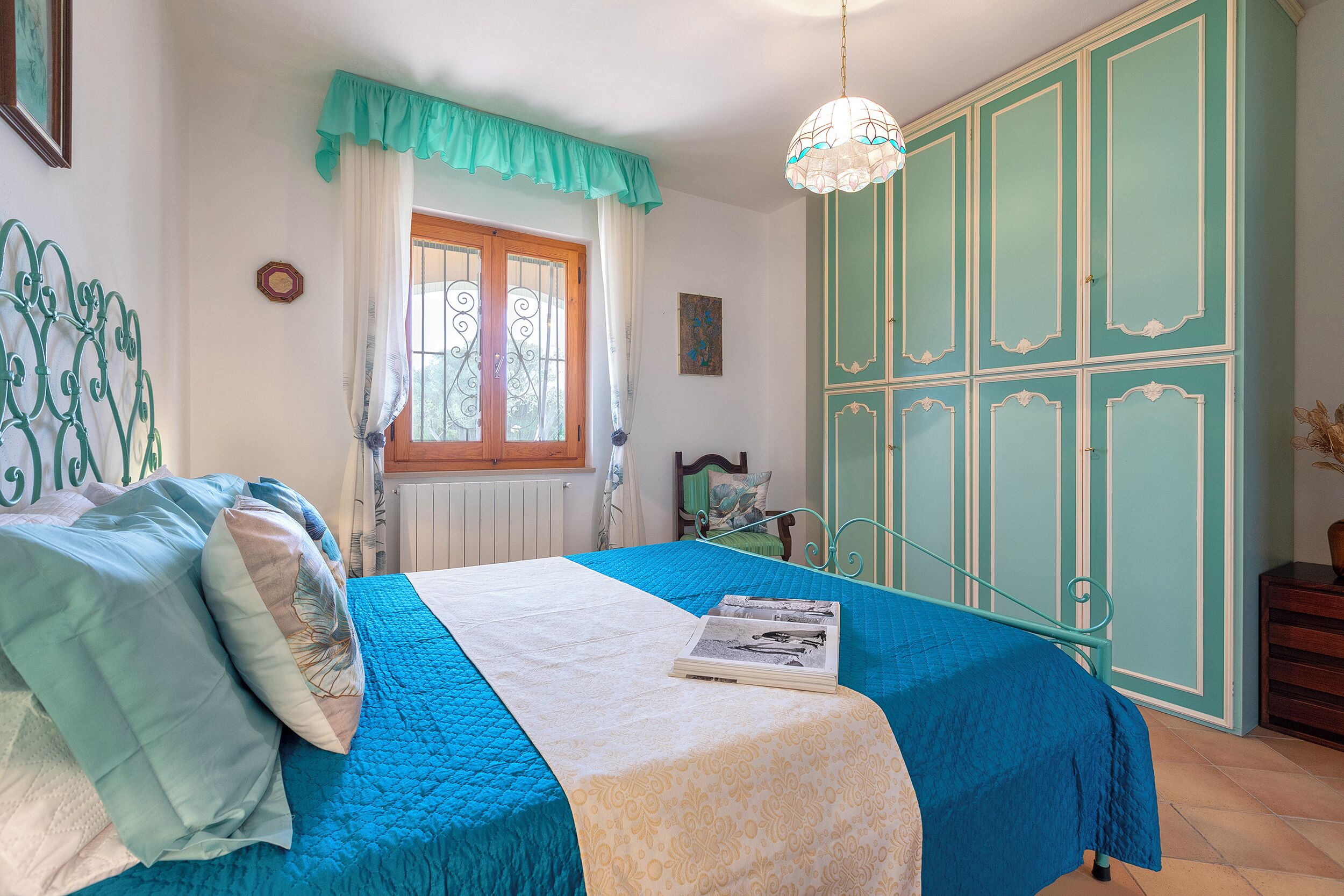 Un dormitorio con cama, una ventana con cortinas, un armario y una lámpara colgante.
