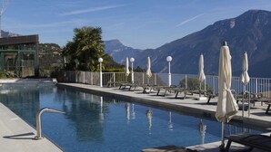 Une piscine entourée d’une clôture, avec des chaises longues et des parasols, et des montagnes en toile de fond.