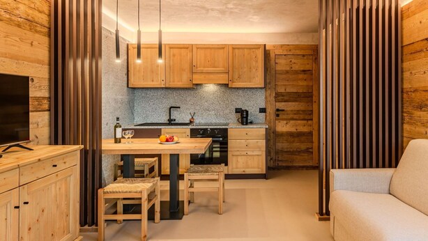 Une cuisine de taille réduite, dotée de meubles en bois, d’un plan de travail en granit et d’un coin repas avec une table et des chaises.