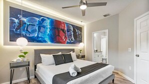 Une chambre moderne avec un grand lit, des tables de chevet, un ventilateur de plafond et une œuvre d’art accrochée au mur.