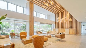 A spacious lobby with large windows, wicker furniture, and a modern wooden accent wall.