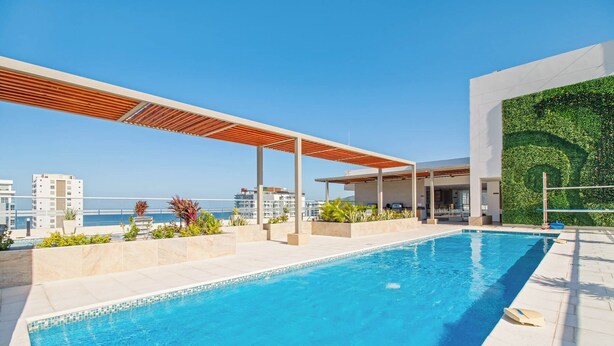 A rooftop swimming pool with a wooden pergola, a green wall, and a view of the sea.