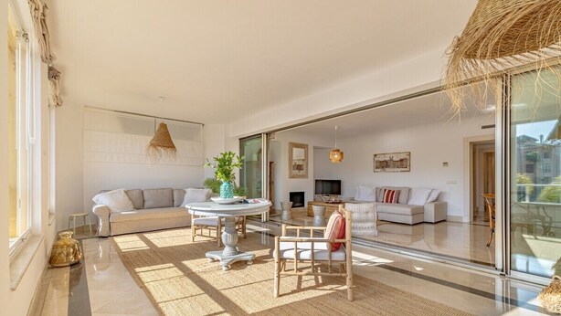 A spacious living room with a large glass door leading to a balcony, a round dining table, and a sofa with a plant.