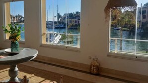 A room with large windows overlooking a marina, a round table with a vase, and a hanging light fixture.