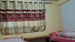 Une chambre avec deux lits, un bureau en bois et une fenêtre ornée de rideaux à motifs.