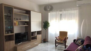 A living room with a TV, wooden entertainment unit, a chair, a sofa, and a potted plant. - Cozy apartment 5 minutes from the metro, ideal for visiting Rome (Roma)