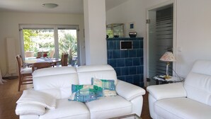 A living room with a white leather sofa, a blue tiled wall, and a glass door leading to a patio. - FERIENHAUS GERDA - Vacation in the sunniest region of Germany (Friesenheim)