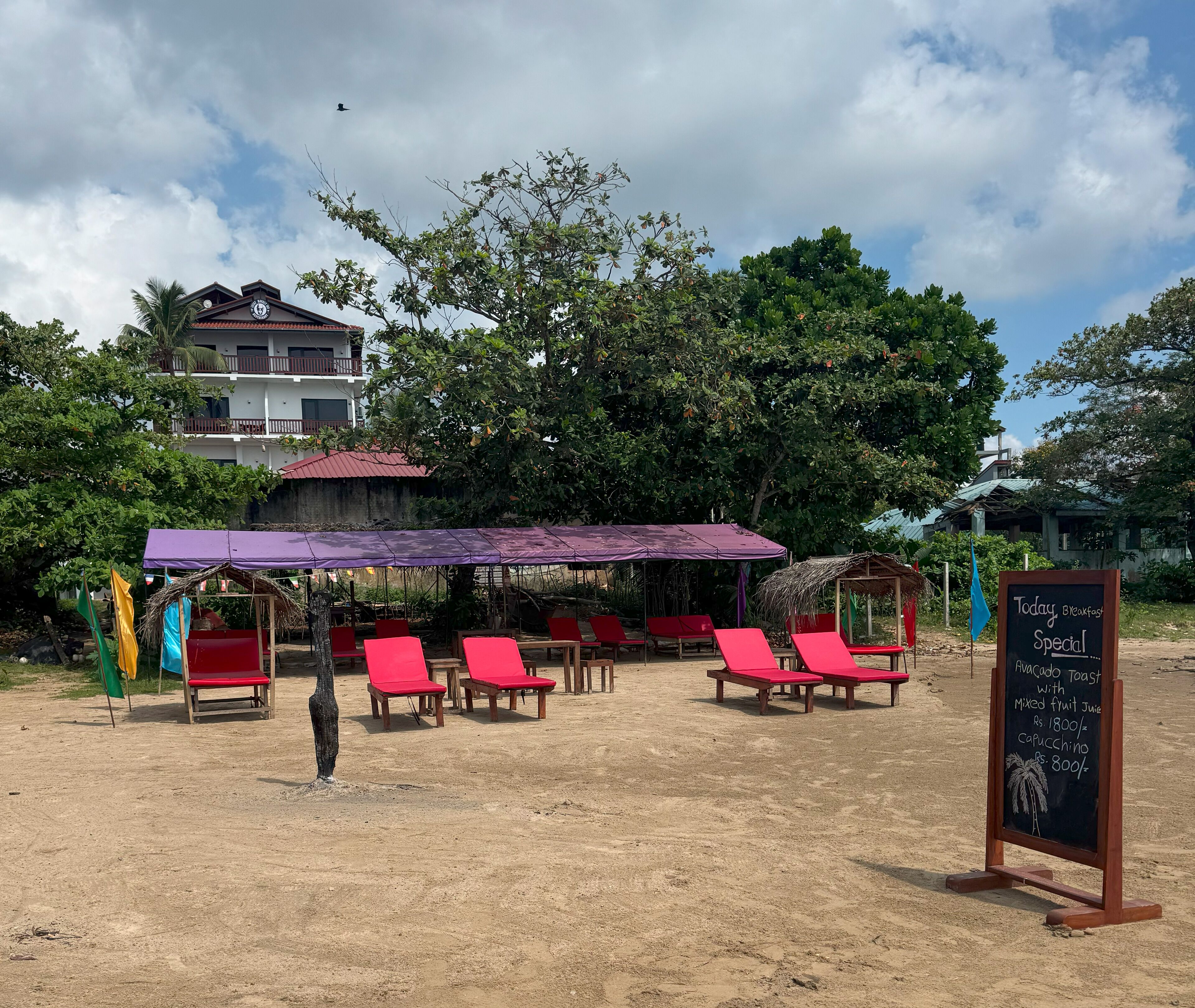 Un café frente a la playa con sillones rojos y un dosel morado.