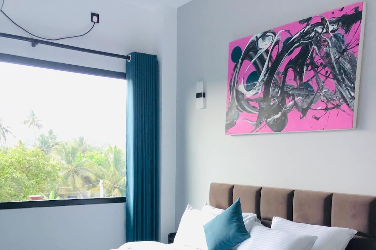 A neatly made bed with a teal and white bedspread, a brown headboard, and a pink abstract painting on the wall.