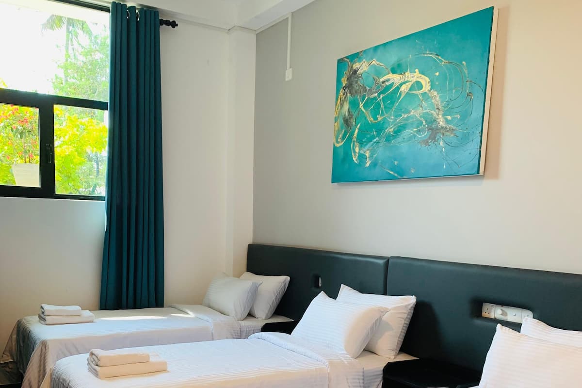 A hotel room with two beds, a large window with curtains, and a painting on the wall.