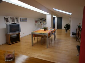 Un vaste espace dédié à la salle à manger, avec une table en bois, des chaises et un téléviseur posé sur un meuble.
