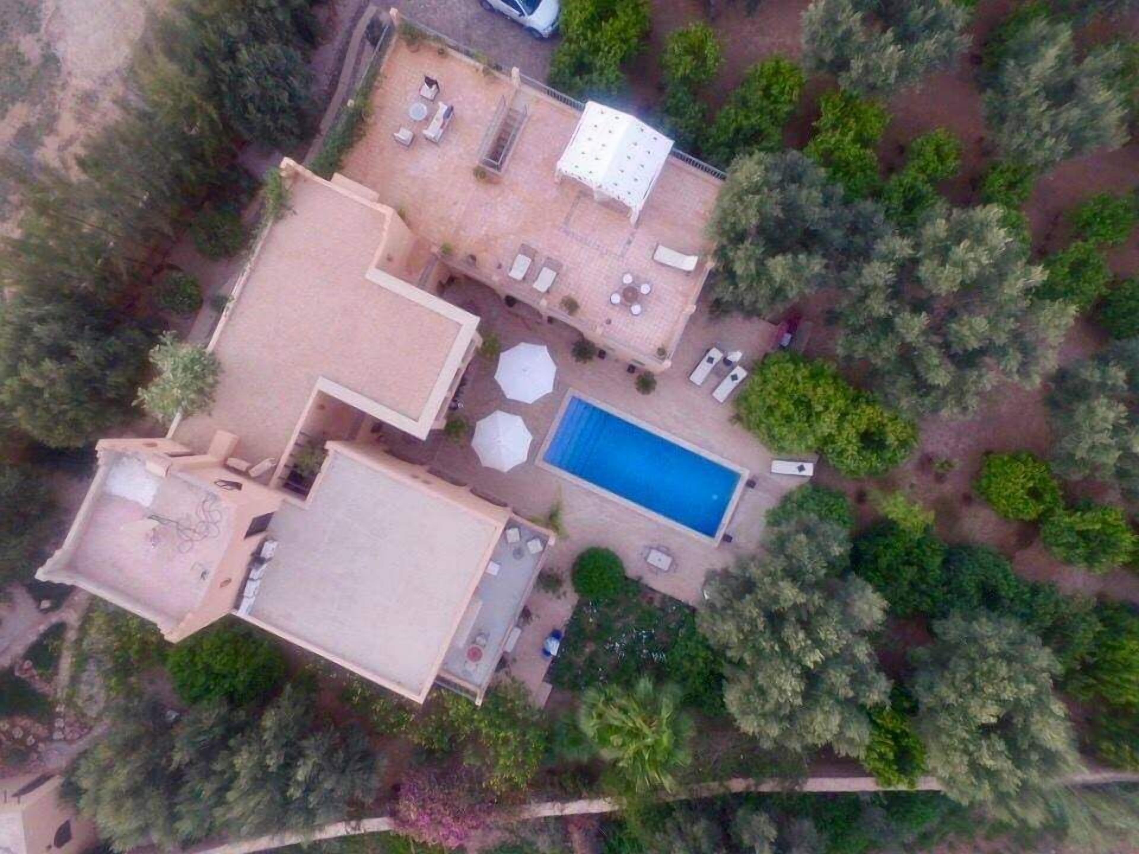 An aerial view of a property with a swimming pool, outdoor seating area, and surrounding greenery.