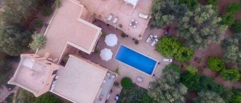 An aerial view of a property with a swimming pool, outdoor seating area, and surrounding greenery.