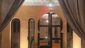 An indoor dining area with a table and chairs, a hanging lantern, and a view through an arched doorway. - Riad Jardin des Orangers (Sidi Borja)
