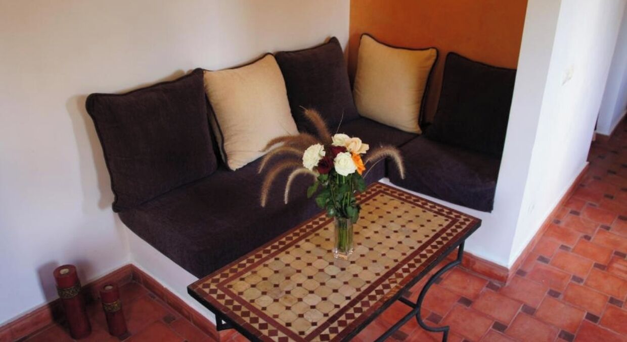 Un sofá marrón oscuro con cojines color beige, una mesa de centro estampada y un jarrón con flores.