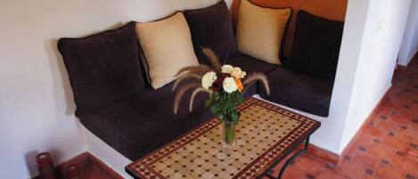 Un sofá marrón oscuro con cojines color beige, una mesa de centro estampada y un jarrón con flores.