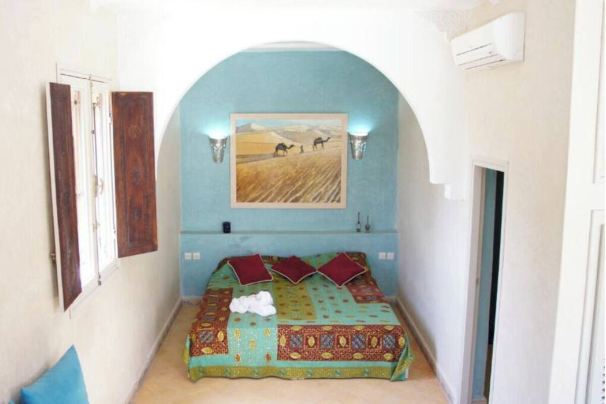 A bedroom with a bed, a painting, and a window.