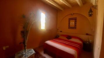 Un dormitorio con cama, ventana, un adorno en la pared y una mesita de noche.