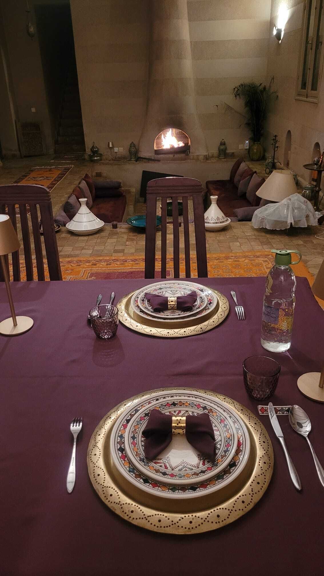 A dining area with a table set for two, featuring traditional tableware and a bottle of water.