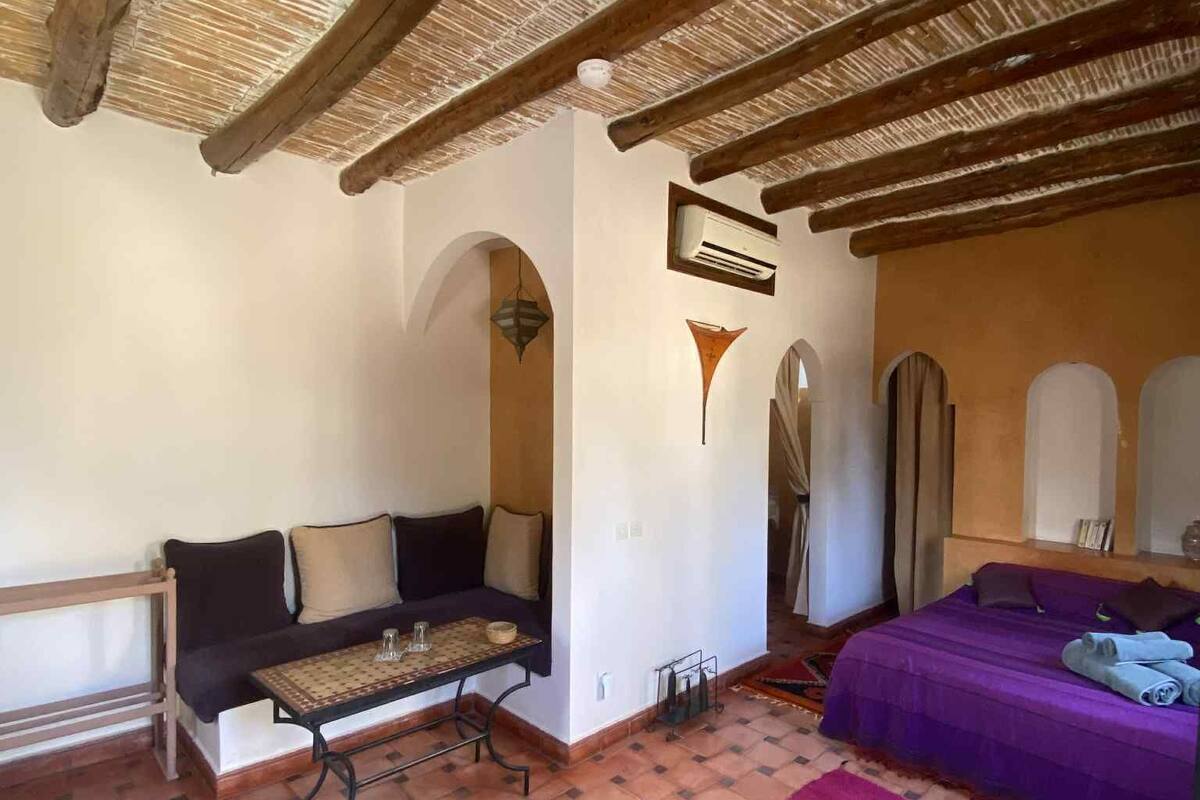 A room with a wooden ceiling, a sofa, a bed, a small table, and a purple rug.