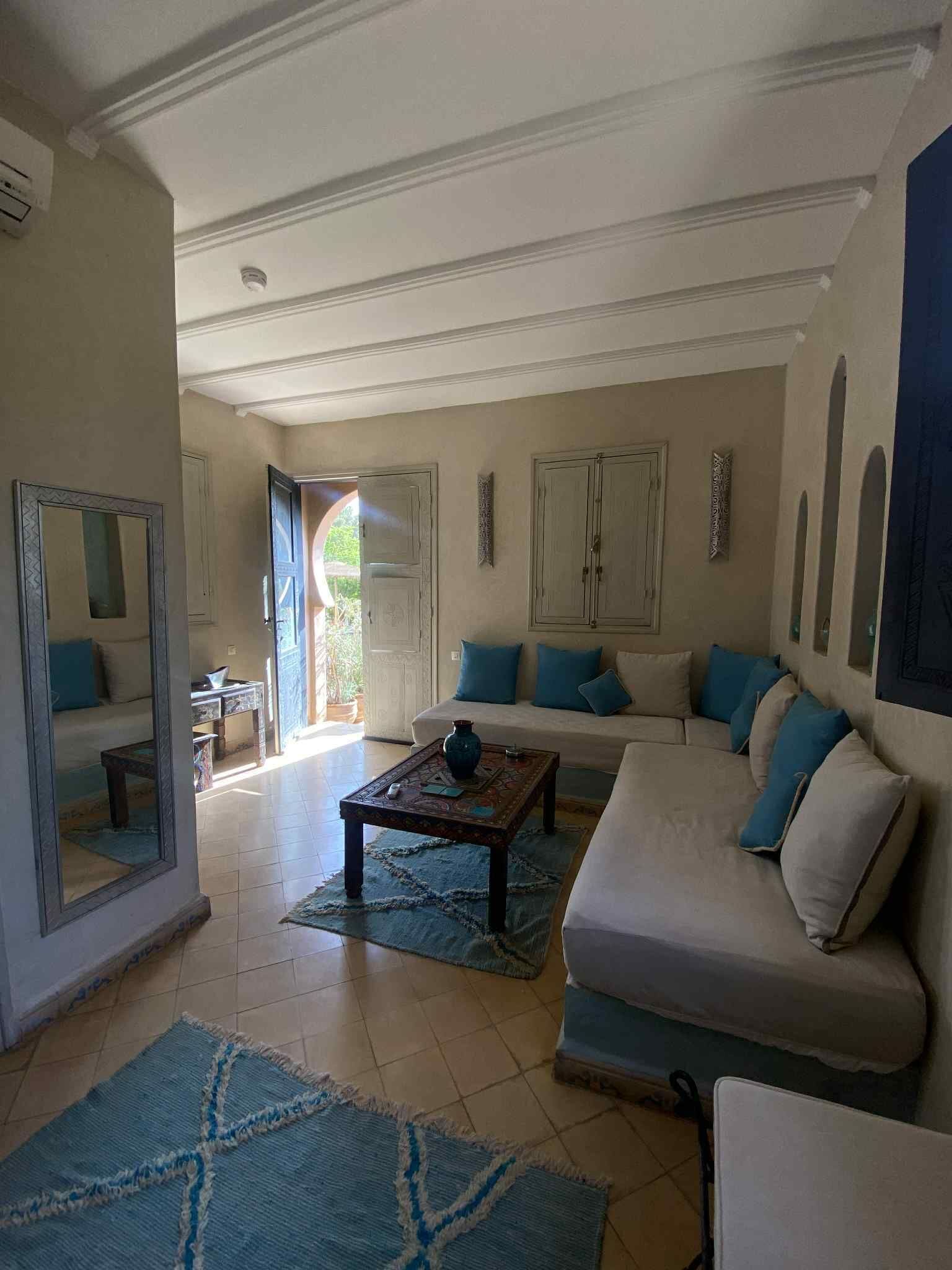 A spacious living room with a large sofa, a coffee table, and a mirror. There is a door leading to an outdoor area.