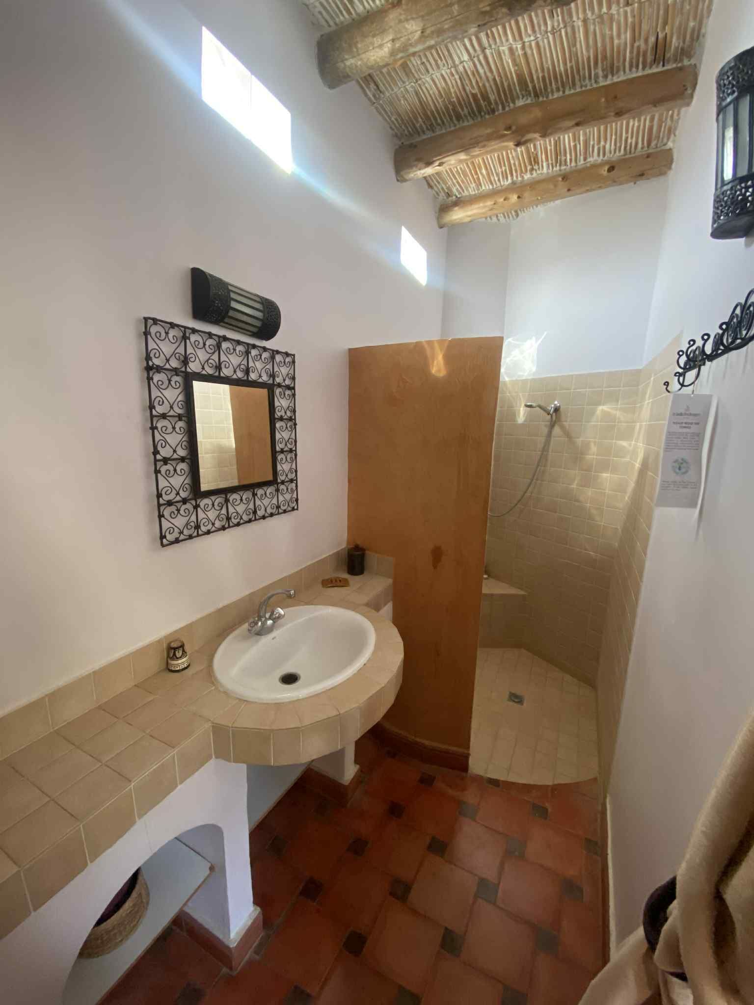 A bathroom with a sink, mirror, shower, and tiled floor.