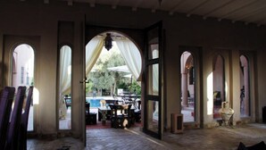 An open doorway leading to an outdoor patio area with a pool, surrounded by arches and a table with chairs. - Riad Jardin des Orangers (Sidi Borja)