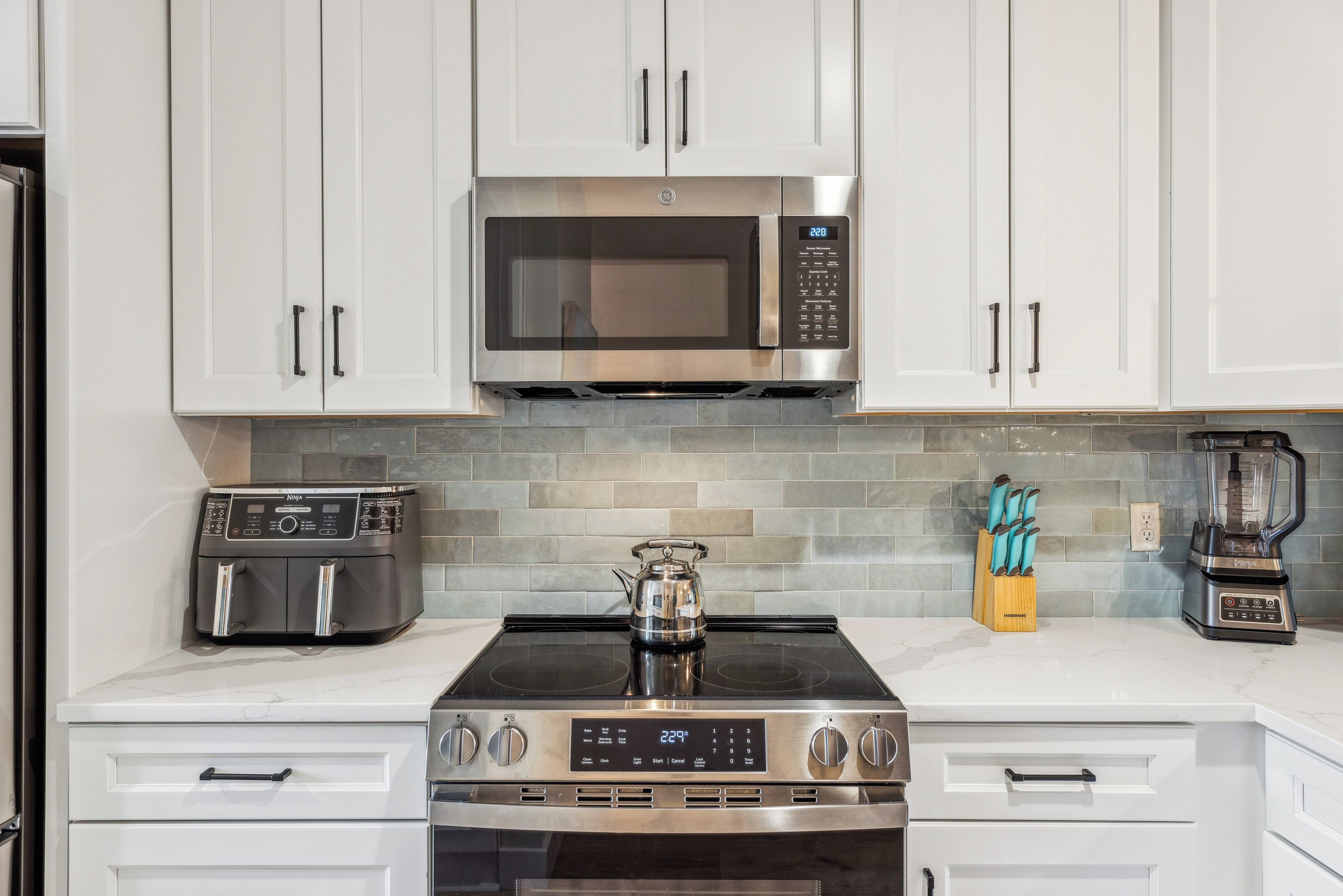 A modern kitchen with white cabinets, a stainless steel microwave, a gas stove, a toaster, and a blender.