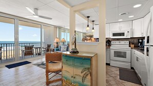 Une cuisine spacieuse avec des meubles blancs, un four à micro-ondes et une cuisinière. Une grande fenêtre donne sur la plage.