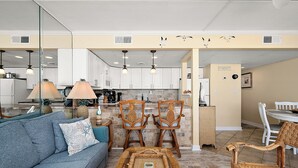 Un salon avec un canapé, des fauteuils, une table basse et une cuisine en arrière-plan.