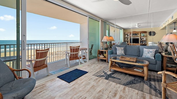 Un vaste espace de vie avec un balcon donnant sur la plage, aménagé avec un canapé, des fauteuils et une table basse.
