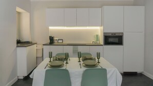 Een moderne keuken met witte kasten, een inbouwoven en een eethoek met een geruit tafelkleed en groene stoelen.