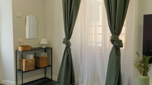 Een kamer met een zwarte console tafel, rieten manden, een spiegel en lichte groene gordijnen vastgebonden aan de bovenkant.