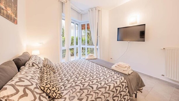 A hotel room with a large bed, a TV mounted on the wall, and a window with curtains.