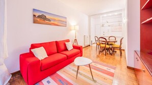 A compact living space with a red sofa, a small round table, and a dining area with wooden chairs.