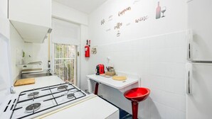 A kitchen with a gas stove, white cabinets, a red sink, and a wall with a coffee and wine theme.
