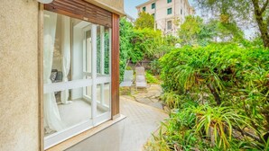 A modern house with a glass door leading to a white interior, surrounded by lush greenery and a stone pathway.