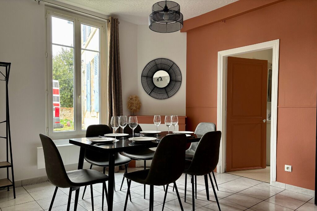 Un coin repas avec une table dressée pour quatre personnes, un lustre moderne et un grand miroir au mur.
