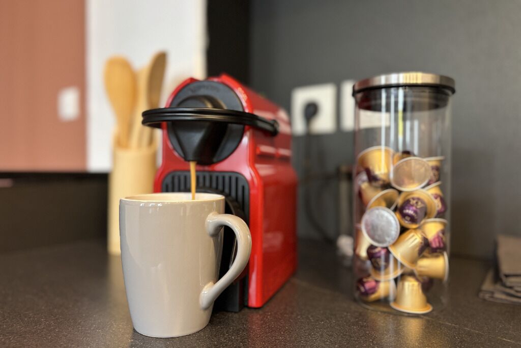 Una cafetera, una taza y un recipiente con cápsulas de café sobre una encimera de cocina.