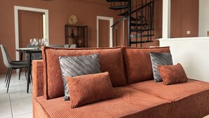 Un salon moderne avec un grand canapé orange, un escalier en colimaçon noir et un coin repas à l’arrière-plan.