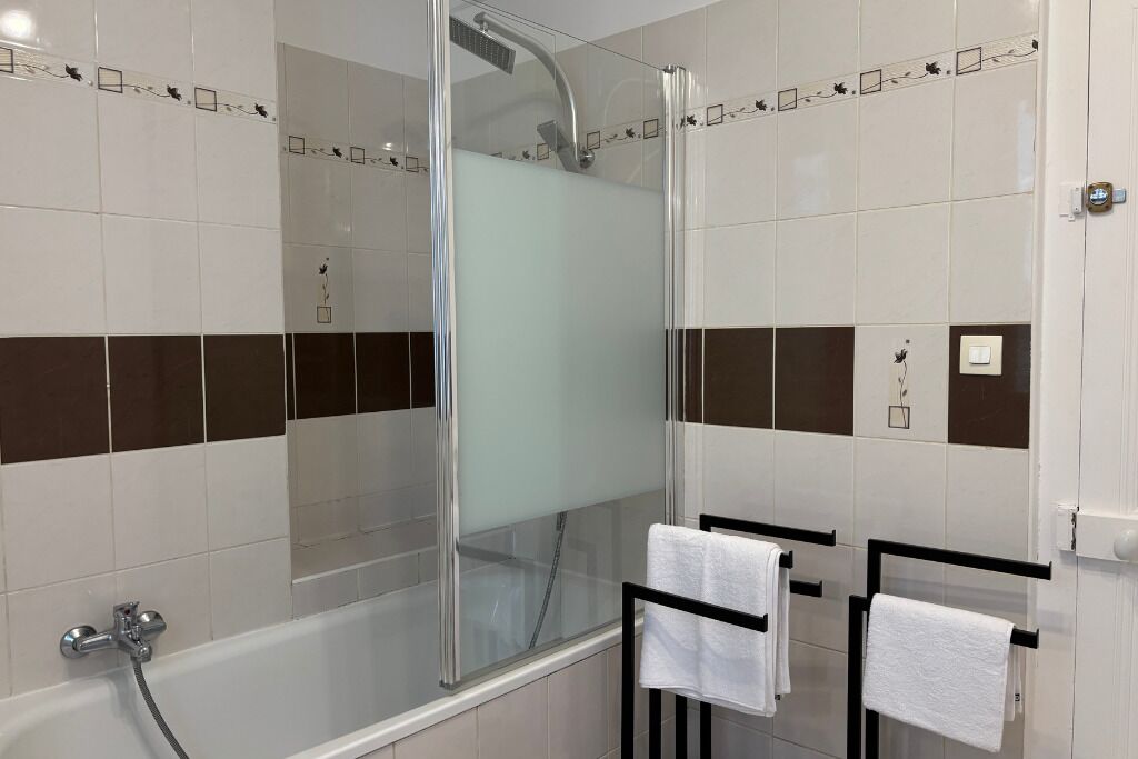 A modern bathroom with a glass-enclosed shower, a bathtub, and two towel racks with white towels.