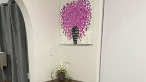 Ein kleiner Essbereich mit einem Holztisch, zwei Stühlen, einer Topfpflanze und einem an der Wand hängenden Kunstwerk.