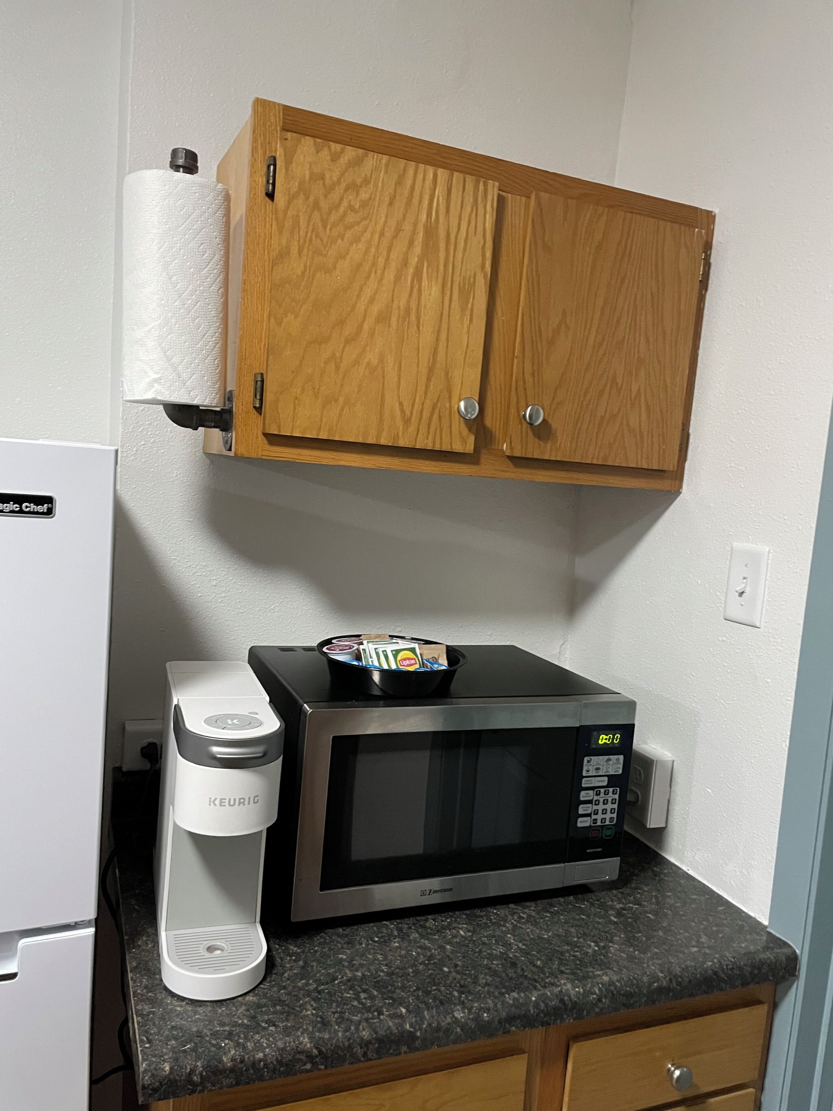 A kitchenette with a microwave, a Keurig coffee maker, and a wooden cabinet above.